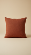 A vibrant terracotta throw pillow, perfectly centered on a soft sand background. The pillow's rich color and texture are...