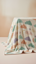 A perfectly centered shot of a patterned nursery blanket from the Whimsical Warmth collection, gently draped over a pastel...
